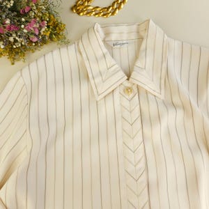May include: A white striped button-down shirt with a chevron detail down the front. The shirt has a collar and a label that reads "Vintage".