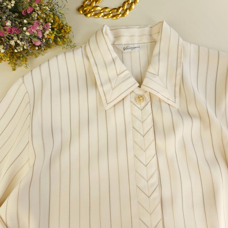 May include: A white striped button-down shirt with a chevron detail down the front. The shirt has a collar and a label that reads "Vintage".