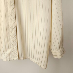 May include: A white button-down shirt with thin vertical black stripes. The shirt has a chevron-shaped detail down the front.