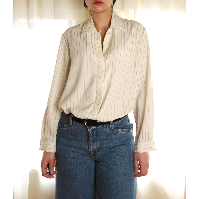 May include: A white striped long-sleeve button-down shirt with a black belt. The shirt has a V-shaped detail on the front.