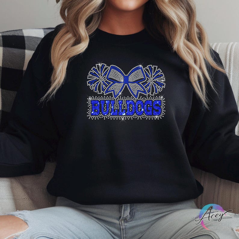 Pu&ograve; includere: Una felpa nera a maniche lunghe con un design grafico centrale realizzato in strass blu e argento. Il disegno raffigura un grande fiocco affiancato da due pon pon, con la parola BULLDOGS scritta in grassetto blu sotto il fiocco.