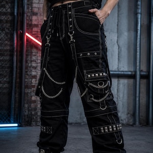 May include: Black cargo pants with white stitching, metal rivets, and chains. The pants feature multiple pockets, straps, and a drawstring waist. The design has a punk or alternative aesthetic.