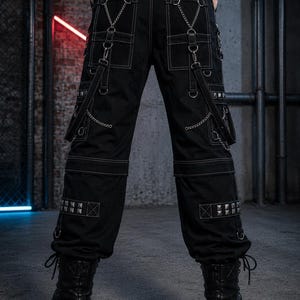 May include: Black cargo pants with white stitching, multiple pockets, and silver chain accents. The pants feature studded details and are paired with black platform boots. The overall style is edgy and alternative.