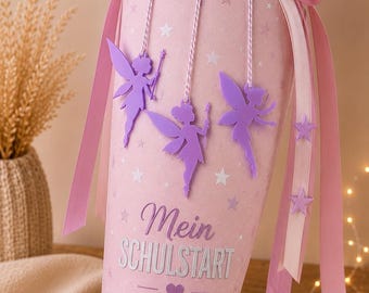 Könnte beinhalten: Eine rosa Schultüte in Kegelform mit dem Text "Mein SCHULSTART" und Stern- und Feendekorationen. Die Tüte ist mit lila Feen-Ausschnitten und rosa Bändern verziert und mit einer rosa Tüllschleife versehen.