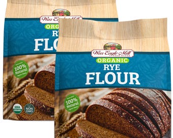 May include: Two bags of War Eagle Mill Organic Rye Flour, each bag showing a loaf of rye bread sliced open. The bags are blue and white with the text "War Eagle Mill Food Group" and "Organic Rye Flour" in black. The bags also have a green USDA Organic seal and a green Non-GMO seal. Each bag has a net weight of 48 oz (1360g).
