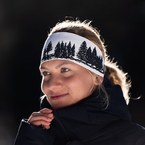 May include: White headband with a black forest silhouette design. The headband is worn by a person with blonde hair. The forest design includes various sizes of pine trees. The headband is made of a soft, flexible material.