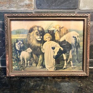 May include: Framed vintage print featuring a child with animals, including a lion, lamb, wolf, and calf. The artwork has a warm color palette with a detailed, ornate gold-toned frame. The print depicts a pastoral scene with a child holding a staff.