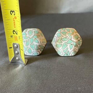 Pu&ograve; includere: Due pomelli esagonali in ceramica con base bianca, decorati con un motivo floreale verde acqua e dettagli dorati. Ogni pomello misura circa 2,5 cm di altezza. Questi pomelli decorativi sono ideali per mobili.