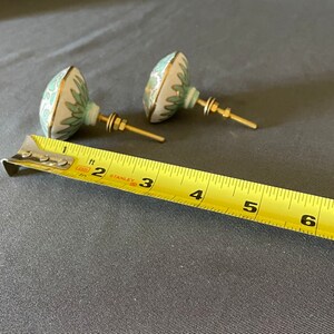 Pu&ograve; includere: Due pomelli decorativi per mobili con base bianca, design floreale turchese e finiture dorate. I pomelli hanno ferramenta in ottone e misurano circa 5 cm di diametro.