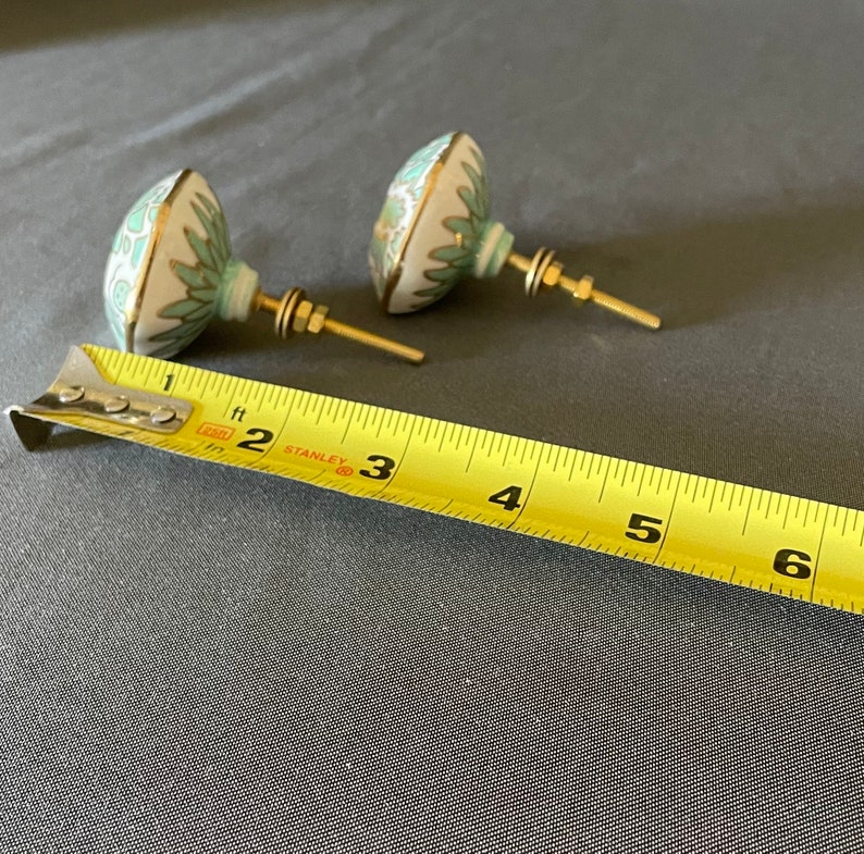 Pu&ograve; includere: Due pomelli decorativi per mobili con base bianca, design floreale turchese e finiture dorate. I pomelli hanno ferramenta in ottone e misurano circa 5 cm di diametro.