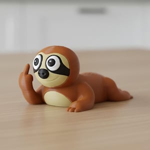 Könnte beinhalten: Eine braune Faultierfigur mit schwarzer Augenmaske und großen, ausdrucksstarken Augen. Das Faultier liegt und zeigt den Mittelfinger. Die Figur befindet sich auf einer hellbraunen Holzoberfläche.