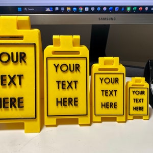 May include: Four yellow plastic sign holders with black text that reads "YOUR TEXT HERE" in different sizes. The sign holders are on a table.
