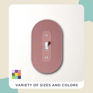 Peut inclure: Un cache-interrupteur rose poudré avec une surface texturée et un interrupteur à bascule blanc. Le couvercle est de forme ovale et monté sur un mur blanc. Le texte "VARIÉTÉ DE TAILLES ET DE COULEURS" est en bas.