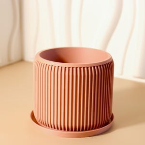 Peut inclure: Un pot de fleurs en terre cuite de couleur terracotta avec un design côtelé et une soucoupe assortie. Le pot est fait d'un matériau lisse et durable et est parfait pour ajouter une touche de style moderne à n'importe quelle maison.