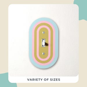 May include: A decorative light switch cover in pastel colours. The cover has an oval design with layers of light blue, pink, and gold. The text "VARIETY OF SIZES" is at the bottom.