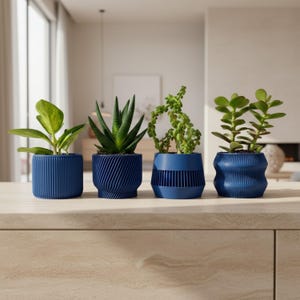 May include: Four small, blue decorative planters with various green plants. The planters have unique textured designs, including vertical lines and swirling patterns. The plants include succulents and leafy greens, adding a touch of nature to the indoor setting.