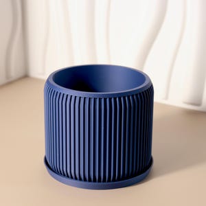 May include: A blue ceramic planter with a ribbed design. The planter is sitting on a light brown surface.
