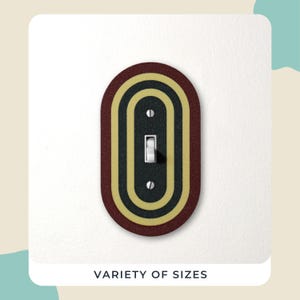 May include: An oval light switch cover with a retro design. The cover has concentric ovals in burgundy, gold, and black, surrounding a white toggle switch. The text "VARIETY OF SIZES" is at the bottom.