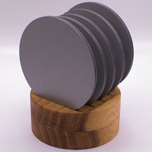May include: A set of six gray round coasters with a wooden holder. The coasters are stacked on top of each other and the holder is made of light brown wood.