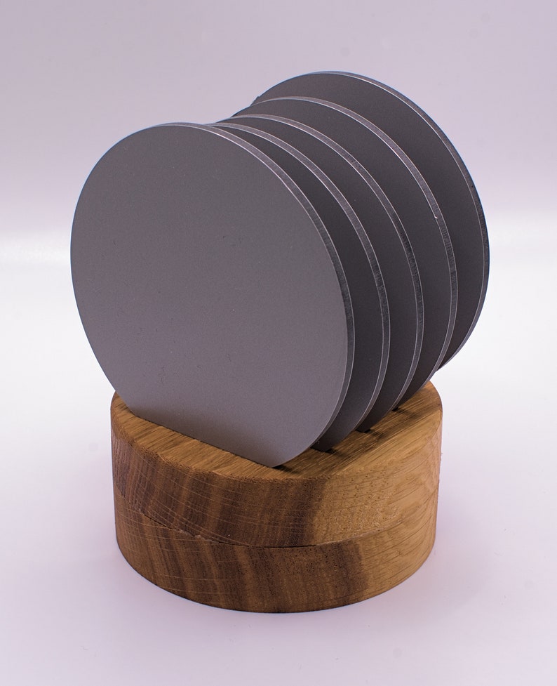May include: A set of six gray round coasters with a wooden holder. The coasters are stacked on top of each other and the holder is made of light brown wood.
