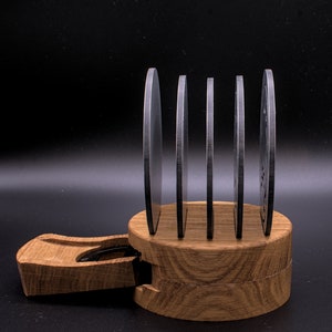 May include: A set of five round, silver coasters with a wood base. The coasters are stacked on top of each other and the base is made of light brown wood.
