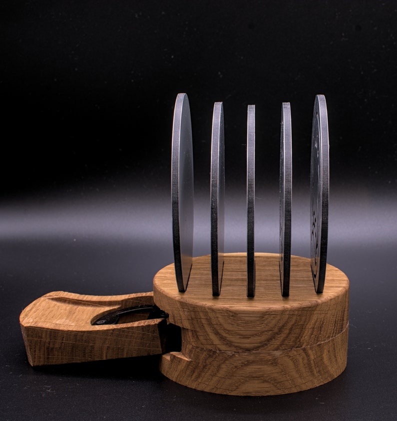 May include: A set of five round, silver coasters with a wood base. The coasters are stacked on top of each other and the base is made of light brown wood.