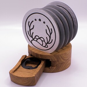 May include: A set of six silver coasters with a black antler design and three dots. The coasters are stacked on a wooden base with a built-in bottle opener.