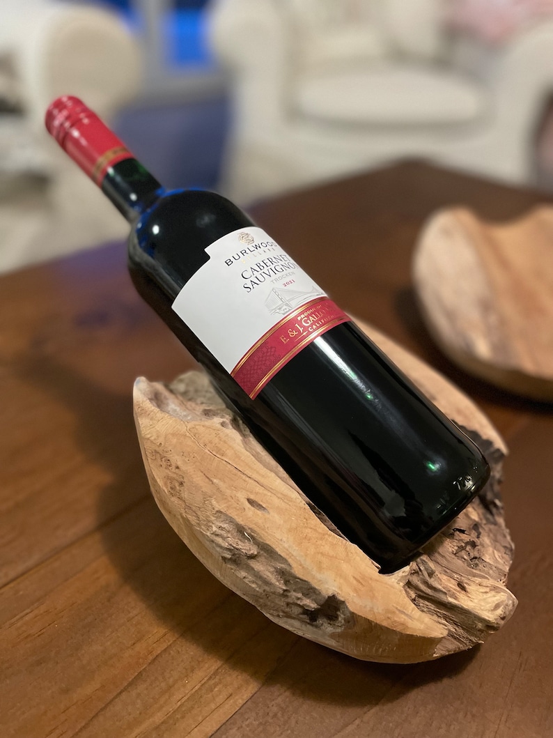 May include: A dark red wine bottle with a red and white label, resting in a natural wood holder. The label reads "BURLWOOD Cabernet Sauvignon". The bottle is angled, showcasing the wine's color and the wood's texture. A decorative piece for wine enthusiasts.
