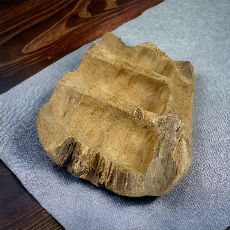 May include: A natural wood serving tray with three carved compartments. The tray has a rough, textured exterior and a smooth interior. The wood grain is visible, and the tray is light brown in color. The tray is on a gray surface.