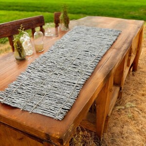 Könnte beinhalten: Ein rustikaler Holztisch mit einem grauen gewebten Tischläufer. Der Tischläufer ist aus natürlichen Materialien gefertigt und hat eine strukturierte Oberfläche.