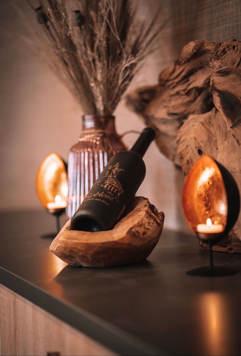 Dieser elegante Weinflaschenhalter aus massivem Teakholz bietet Platz für drei Weinflaschen und verbindet natürliche Schönheit mit praktischem Design. Jeder Halter wird aus einem einzigartigen Stück Holz gefertigt – keine Maserung gleicht der anderen, sodass du immer ein echtes Unikat erhältst.

Das warme, goldbraune Teakholz sorgt für eine edle, natürliche Optik, die in jeder Umgebung ein Blickfang ist – ob in der Küche, im Wohnzimmer oder im Weinkeller.