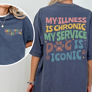 Może przedstawiać: Granatowa koszulka z napisem "MY ILLNESS IS CHRONIC, MY SERVICE DOG IS ICONIC" w kolorowych literach. Koszulka ma również napis "CHRONICALLY ICONIC" z przodu. Koszulka ma luźny krój.