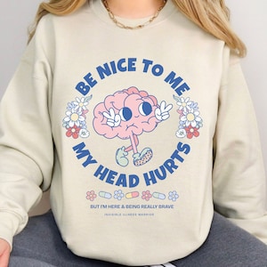May include: Beige sweatshirt with a cartoon brain wearing a peace sign and the text "Be nice to me, my head hurts. But I'm here & being really brave. Invisible illness warrior."