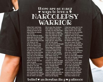 Może przedstawiać: Czarny t-shirt z białym napisem. Z przodu widnieje napis 'love is meeting us where we are'. Z tyłu znajduje się tekst 'there are so many ways to love a NARCOLEPSY WARRIOR' oraz długa lista opisowych stwierdzeń.