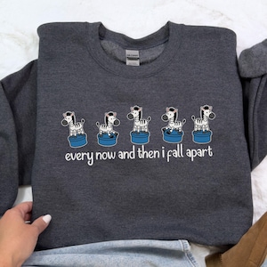 Puede incluir: Sudadera gris oscuro con un diseño caprichoso de cinco cebras sobre plataformas azules. El texto blanco debajo dice "every now and then i fall apart". La sudadera está hecha de un material suave.