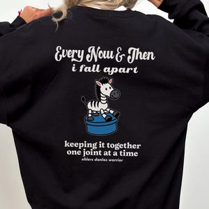 May include: Black sweatshirt with the text "Every Now & Then I fall apart" and a zebra graphic. Below the graphic is the text "keeping it together one joint at a time, ehlers danlos warrior."