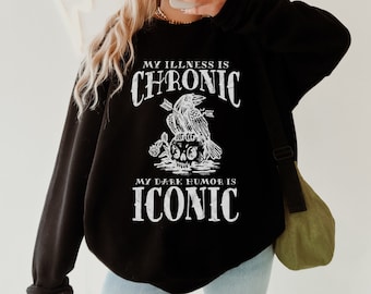 May include: Black sweatshirt with a white graphic print of a raven perched on a skull with the text "My illness is chronic, my dark humor is iconic".