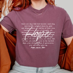 Puede incluir: Una camiseta morada con un estampado gráfico blanco que dice "there are days that feel heavier. each step. each breath. weighed down by pain and fatigue. these are battles of their own. testing every ounce of strength. yet. through every hope the weight you carry. bring the challenges you face. it's not a journey you chose. but it's one you endure, even on the hardest days. your strength rises. it perseveres. you will never give up. hope never dies."