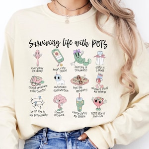 May include: A cream-coloured sweatshirt with the text "Surviving life with POTS" and a series of illustrations depicting common symptoms and experiences associated with Postural Orthostatic Tachycardia Syndrome (POTS).