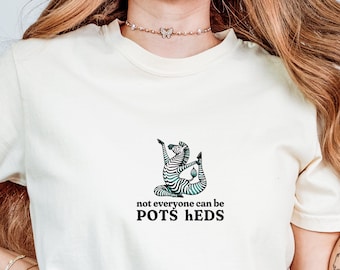 May include: A white t-shirt with a black and white zebra illustration in a yoga pose. The text "not everyone can be POTS HEDS" is printed below the zebra.