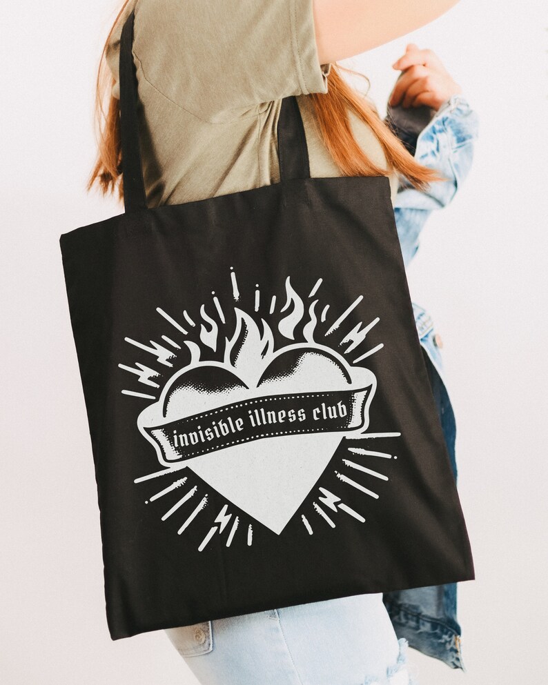 May include: Black tote bag with a white graphic of a heart on fire with the text "invisible illness club" on a banner.
