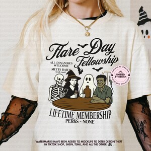 Könnte beinhalten: Cremefarbenes T-Shirt mit einem Halloween-Motiv. Das Design zeigt den Text "Flare Day Fellowship" mit Illustrationen eines Skeletts, einer Hexe, eines Geistes und Frankensteins Monsters. Das Shirt hat auch den Text "Lifetime Membership Perks - None".