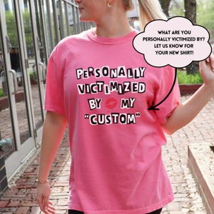 Peut inclure: T-shirt rose avec le texte "PERSONALLY VICTIMIZED BY MY "CUSTOM"" et un graphique de lèvres roses.