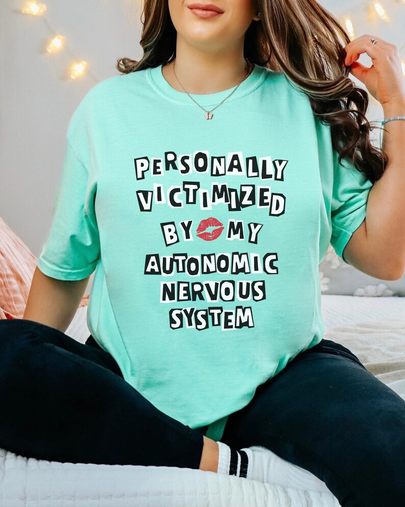May include: A turquoise t-shirt with the text "PERSONALLY VICTIMIZED BY 💋 MY AUTONOMIC NERVOUS SYSTEM" printed in black.