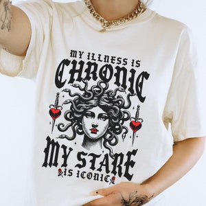Könnte beinhalten: Weißes T-Shirt mit einer schwarz-weißen Grafik von Medusa mit dem Text "My illness is chronic, my stare is iconic."