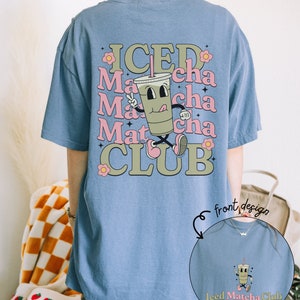 May include: A light blue oversized t-shirt with a cartoon illustration of a green iced matcha drink with the text "ICED Matcha CLUB" on the back. The front of the shirt has a smaller version of the cartoon drink with the text "Iced Matcha Club".