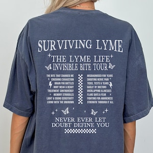 Puede incluir: Una camiseta azul oscuro con texto blanco que dice "Surviving Lyme", "The Lyme Life" y "Invisible Bite Tour". El texto está rodeado de pequeñas mariposas blancas y patrones a cuadros. La camiseta también incluye una lista de síntomas y desafíos asociados con la enfermedad de Lyme.