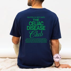 Op de afbeelding: Marineblauw T-shirt met groene tekst: "GLUTEN. IS. NOT. SAFE. THE CELIAC DISEASE Club." Het T-shirt bevat ook een beschrijving van coeliakie. Casual stijl.