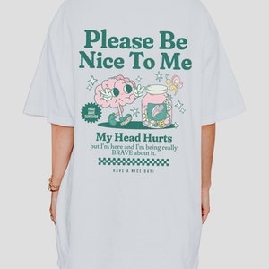 May include: White t-shirt with a green and pink graphic of a brain in a jar with the text "Please Be Nice To Me", "My Head Hurts but I'm here and I'm being really BRAVE about it." and "HAVE A NICE DAY!"