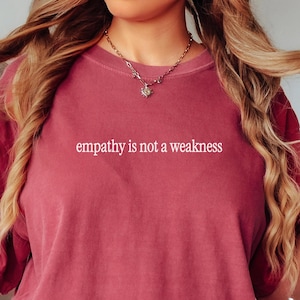 May include: A maroon t-shirt with the text "empathy is not a weakness" printed in white on the front.